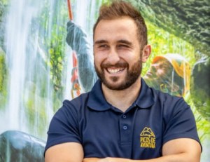 Man smiling in navy shirt with nature background.