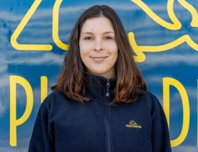 Woman in blue jacket smiling in front of a blue and yellow background.
