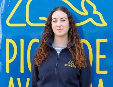 Person with curly hair in front of a blue sign with yellow text.