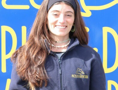 Person smiling in front of a blue and yellow sign wearing a dark jacket.