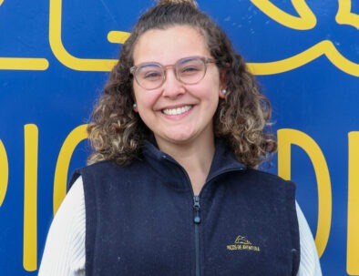 Smiling person in glasses and blue vest against a blue and yellow background.