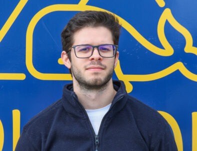Man with glasses and beard in front of blue-yellow whale graphic.