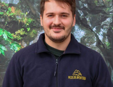 Man smiling in front of a nature-themed background, wearing a navy jacket with a logo.