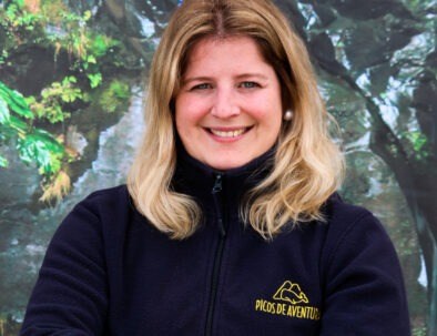 Woman smiling, wearing a navy jacket with outdoor backdrop.