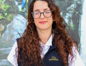Woman with curly hair and glasses standing in front of a nature backdrop.