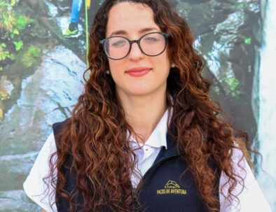 Woman with curly hair and glasses standing in front of a nature backdrop.