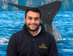 Smiling man in hoodie with whale tail in ocean background.