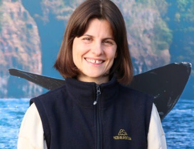 Woman smiling in front of ocean backdrop with whale tail visible.