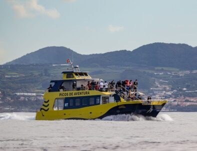 Yellow tour boat with passengers on a scenic cruise near mountains.