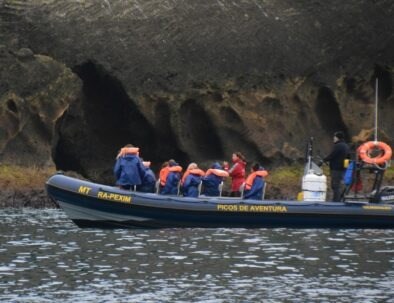 People in life jackets on a tour boat near rocky shore.