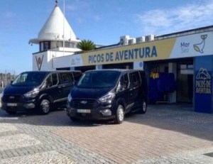 Two black vans parked outside Picos de Aventura building on a sunny day.
