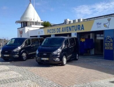 Two black vans parked outside Picos de Aventura building on a sunny day.