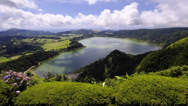Scenic view of a lake surrounded by lush greenery under a partly cloudy sky.