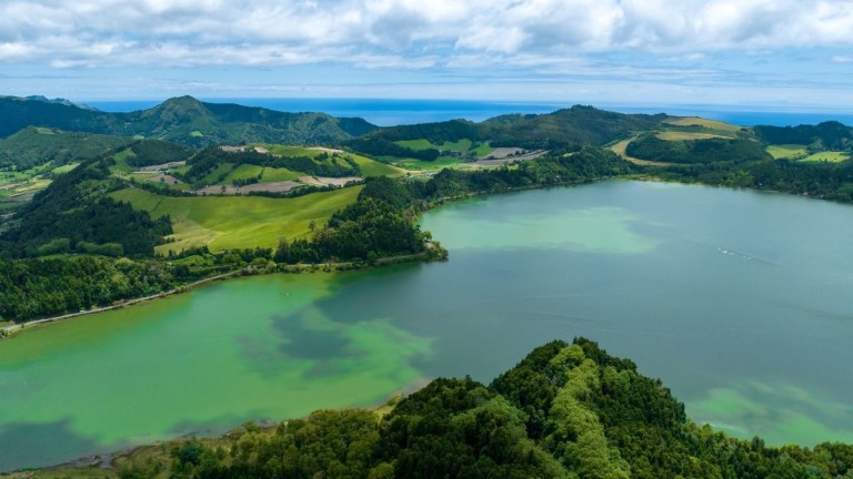 Aerial view of a lush green landscape with a large lake and distant hills under a partly cloudy sky.