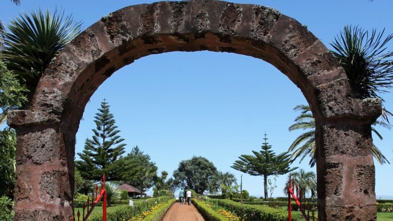 Stone arch framing a garden path with trees and sky.