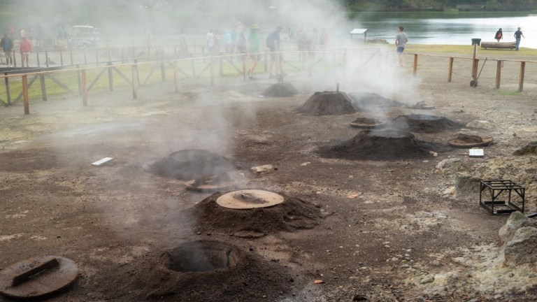 Steaming fumaroles with people and a lake in the background.