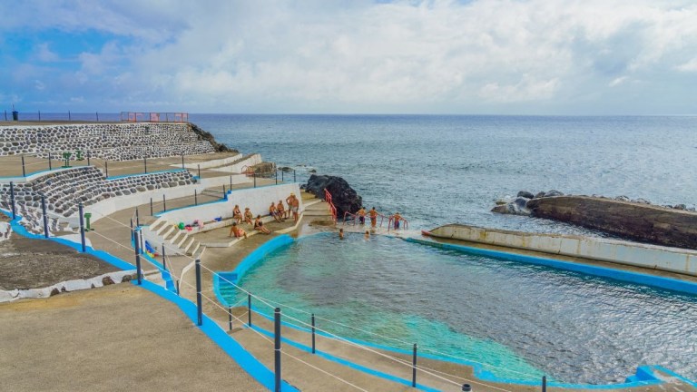 Outdoor ocean pool with people swimming, surrounded by rocky shoreline.