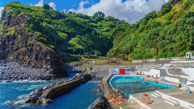 Coastal pool with lush green cliffs and blue sky.