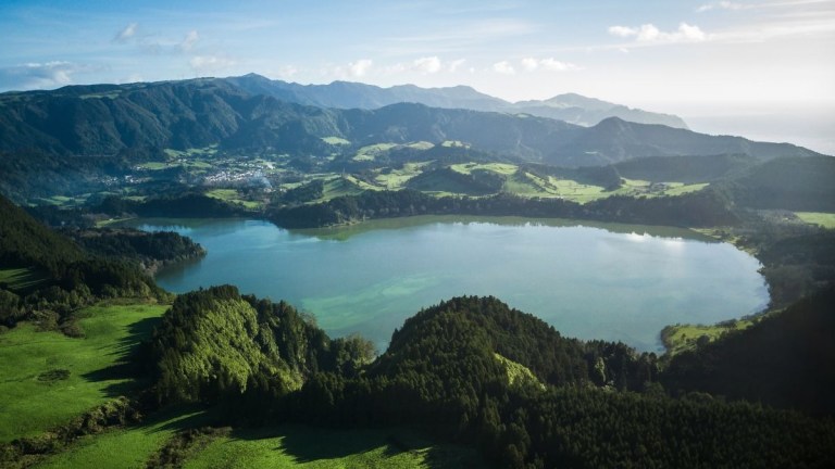 Aerial view of a green valley with a large circular lake and surrounding hills.