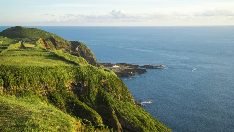 Scenic view of green cliffs overlooking a calm ocean under a cloudy sky.