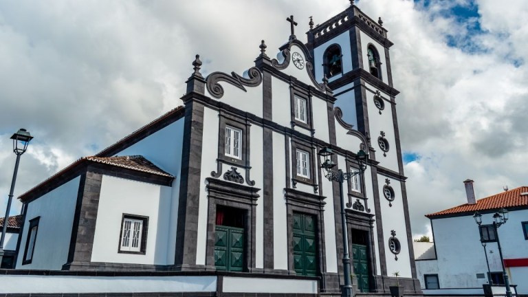 Baroque-style church with green doors and twin bell towers under a cloudy sky.