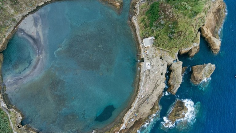 Aerial view of a circular coastal lagoon with surrounding rocky cliffs.