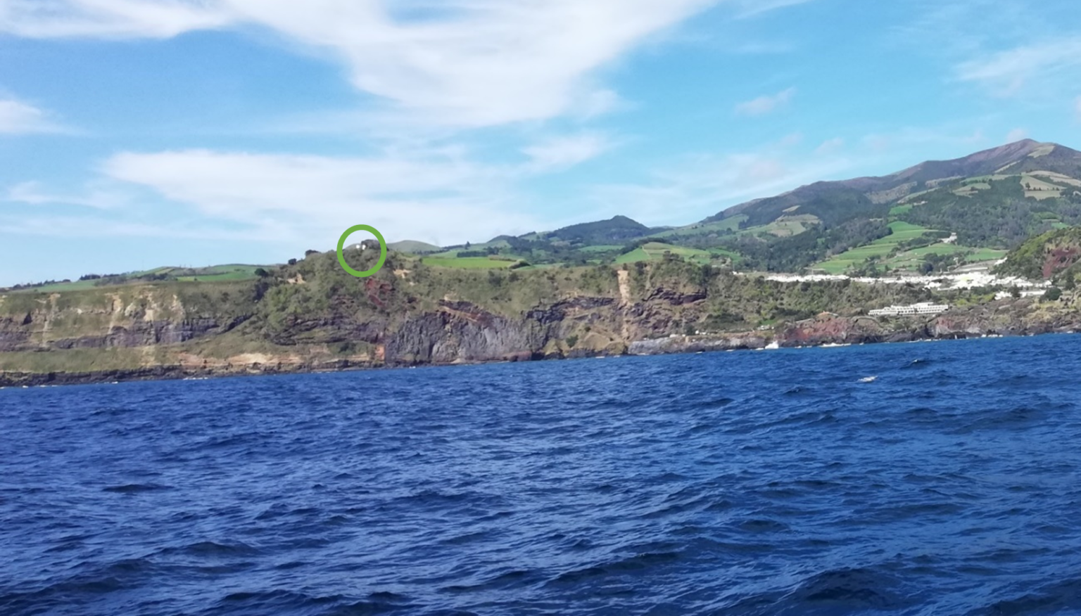 Coastal landscape with green hills and blue ocean under a cloudy sky.