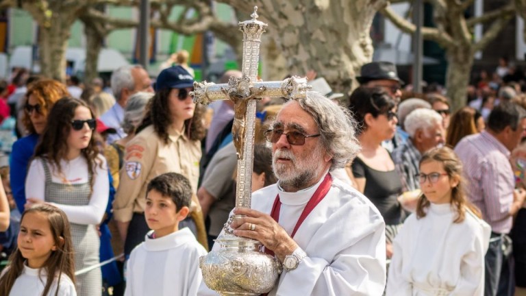 Man in religious procession holding a cross, surrounded by crowd.