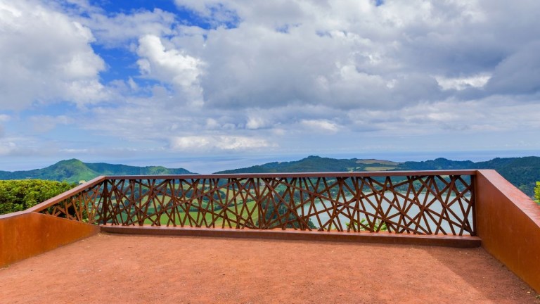 Scenic view from a terrace overlooking hills and a lake under a cloudy sky.