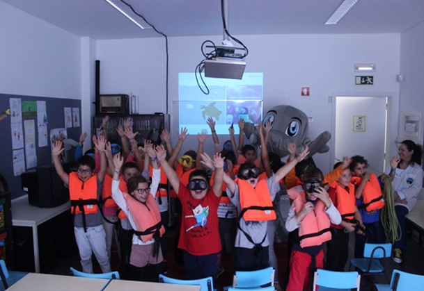 Children wearing life jackets and VR headsets raise hands in a classroom.