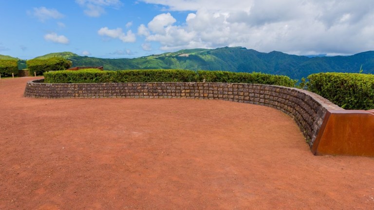 Scenic viewpoint with red soil path, stone wall, and mountain view.