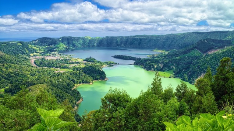 Lush landscape with two lakes surrounded by green hills under a partly cloudy sky.