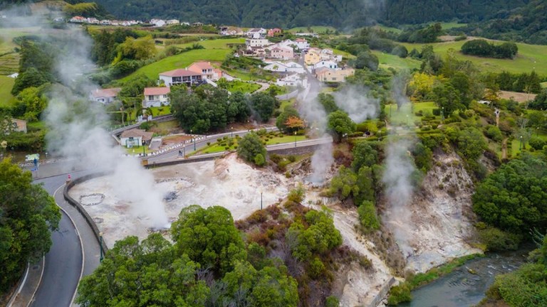 Aerial view of a village with steaming geothermal vents and lush greenery.