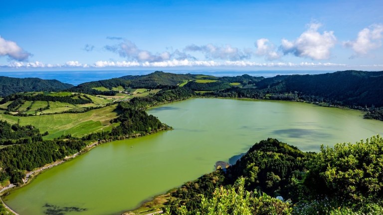 Scenic view of a green lake surrounded by lush hills and trees under a clear blue sky.