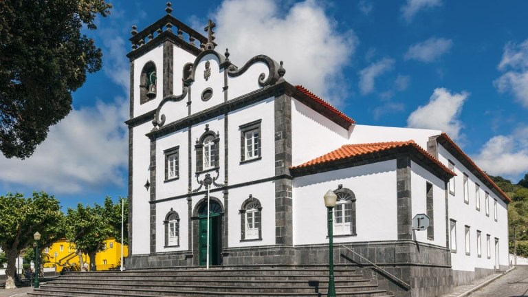 White church with black trim and bell tower under a blue sky.