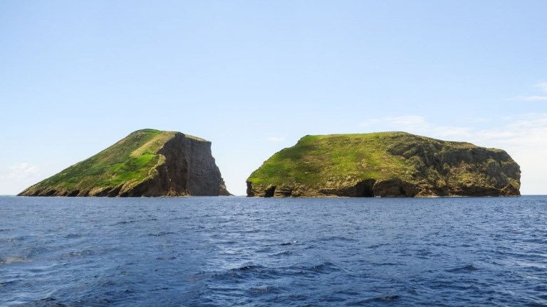 Two green, rocky islands in a blue ocean under a clear sky.