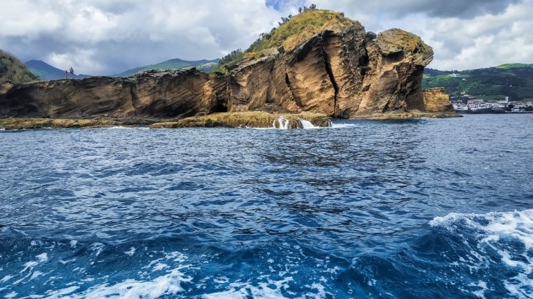 Rocky coastal landscape with blue ocean and partly cloudy sky.