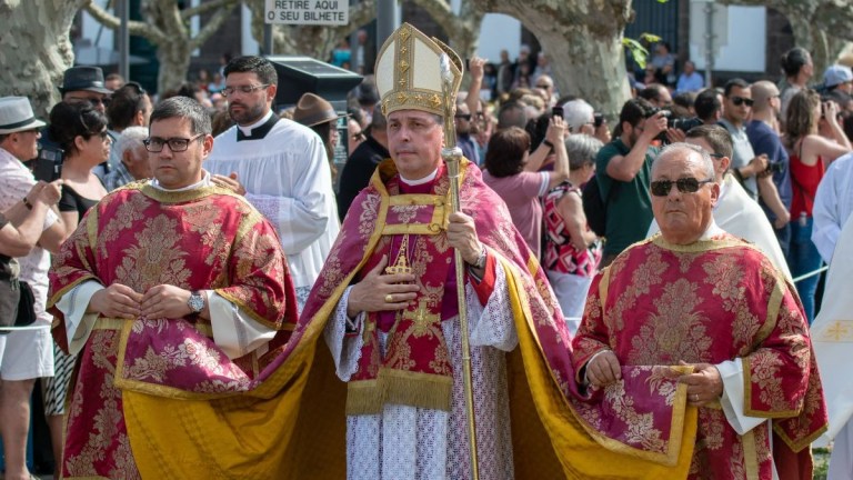 Religious procession with a bishop and priests in ornate red vestments.