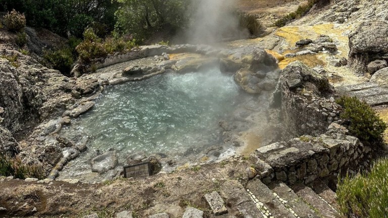 Natural hot spring with steam rising and surrounding rocks.