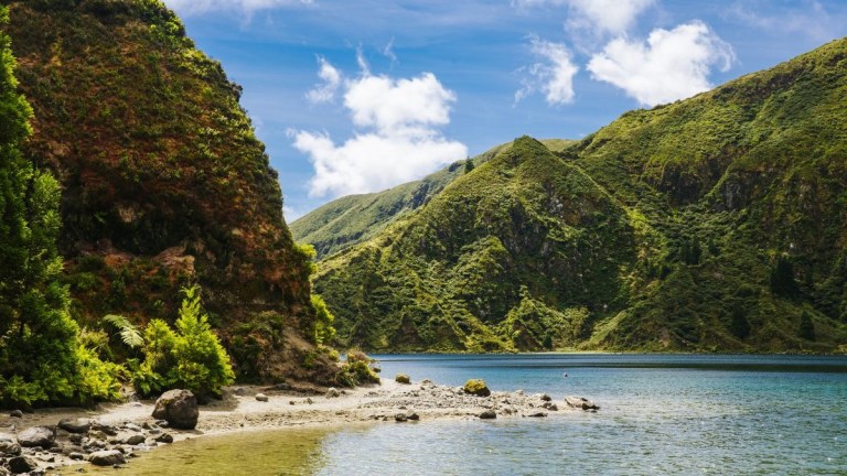 Scenic view of a lake surrounded by lush green hills under a blue sky with clouds.