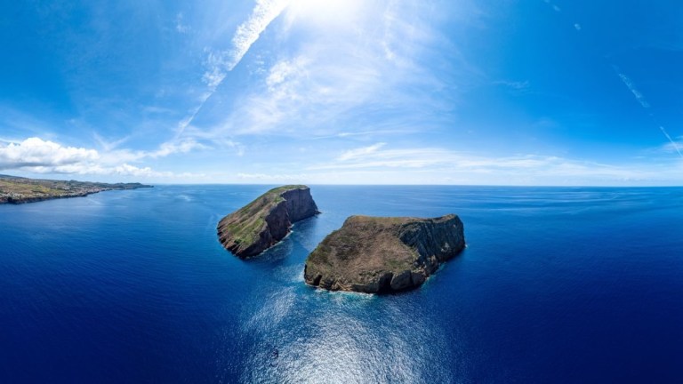 Two rocky islands in a bright blue ocean beneath a clear sky.