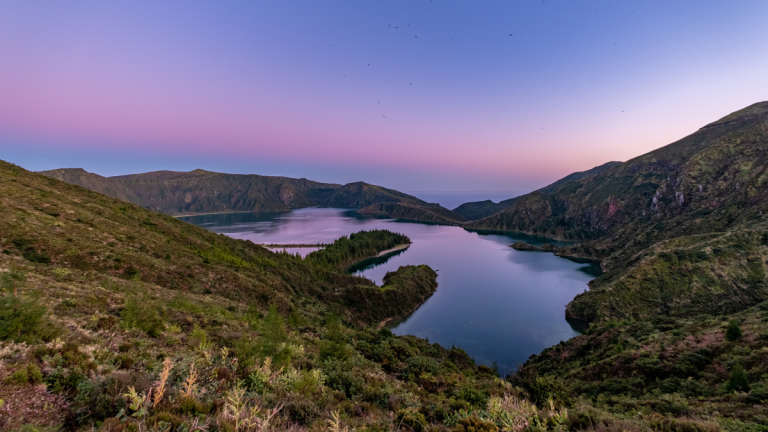 Lake surrounded by rolling hills at sunset, with a clear sky.