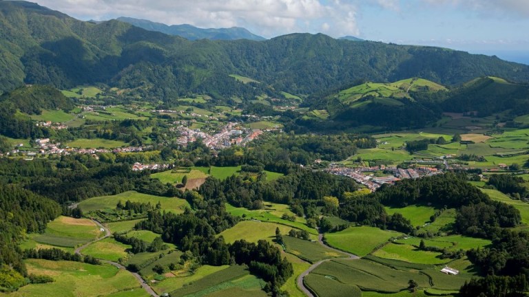 Aerial view of a lush green valley with scattered buildings and surrounding mountains.