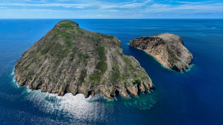 Aerial view of two rocky islands in a calm blue ocean under a clear sky.