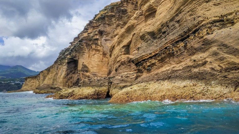 Coastal cliff with layered rock formations above turquoise sea.
