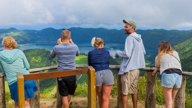 People enjoy a scenic view of mountains and lake from a wooden fence.