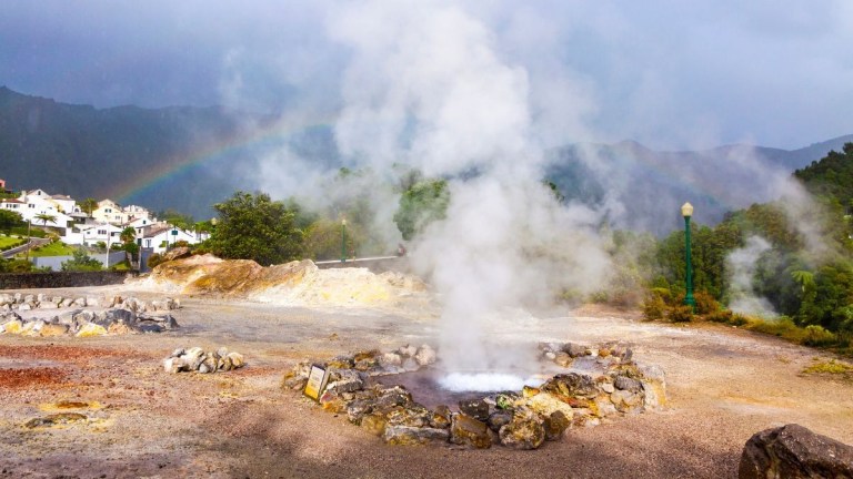 Steam rising from a geothermal area with a rainbow in the background.