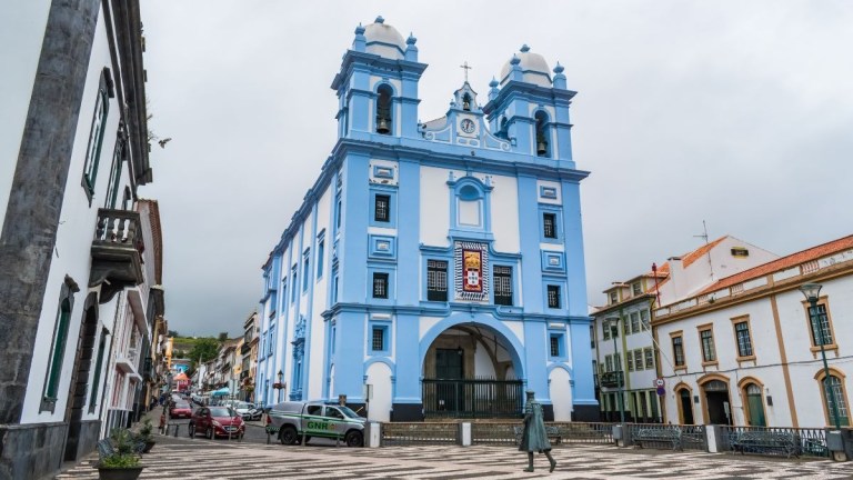 Blue church with twin towers on a cloudy day in a town square.