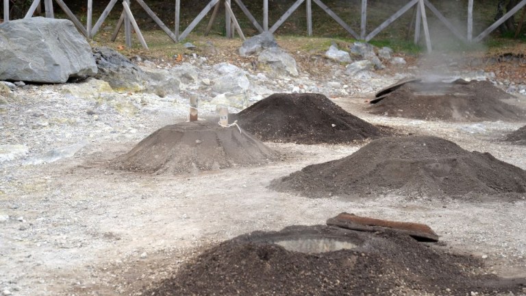 Piles of volcanic soil with scattered rocks and a wooden fence.