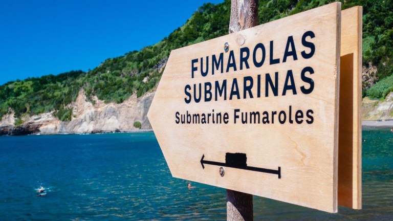 Sign for submarine fumaroles near a scenic coastal area.